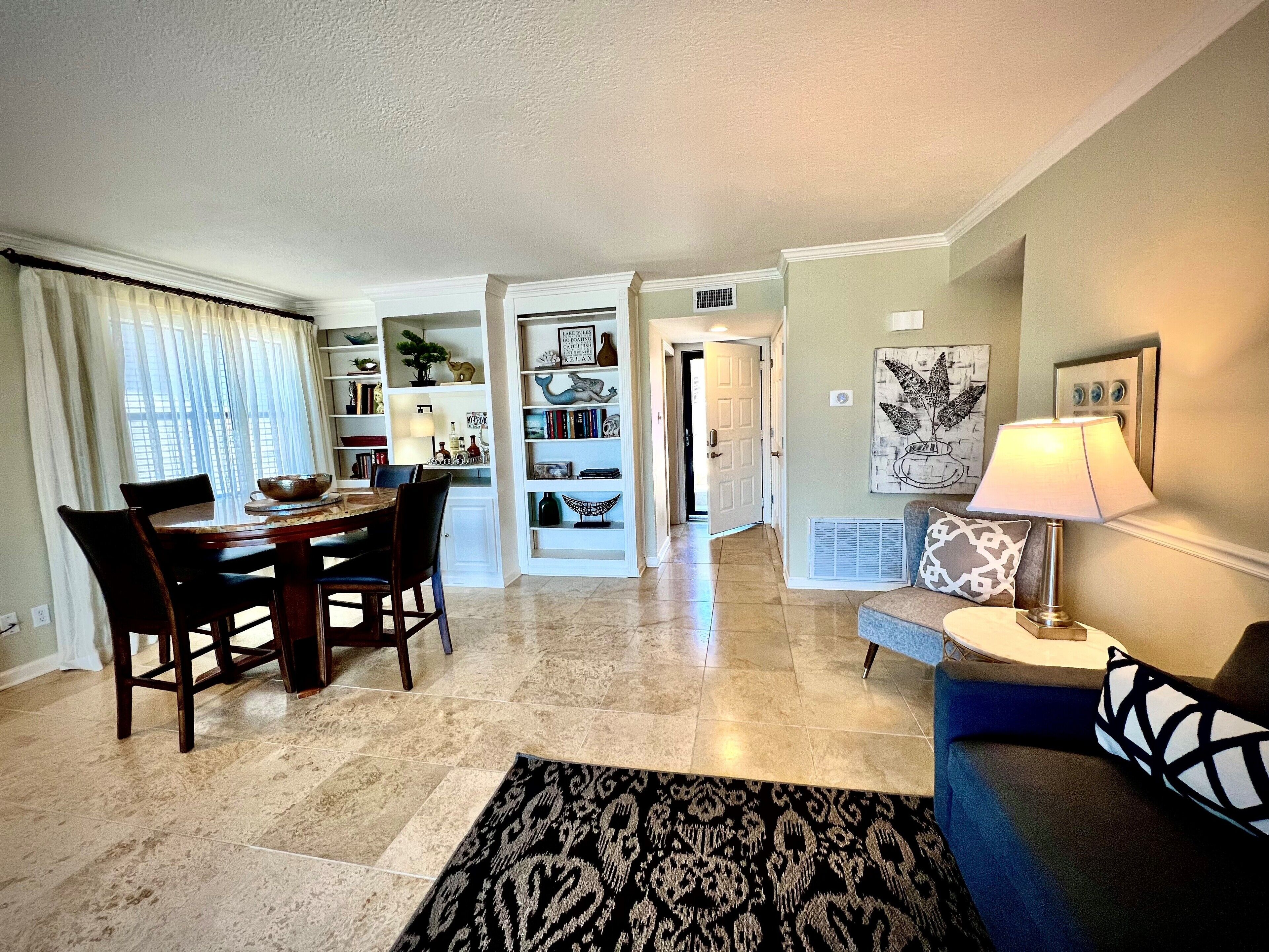 A dining area with a table and chairs, a living room with a sofa and a lamp, and a hallway leading to another room.