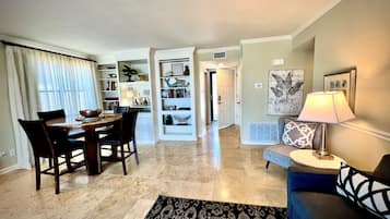 A dining area with a table and chairs, a living room with a sofa and a lamp, and a hallway leading to another room.