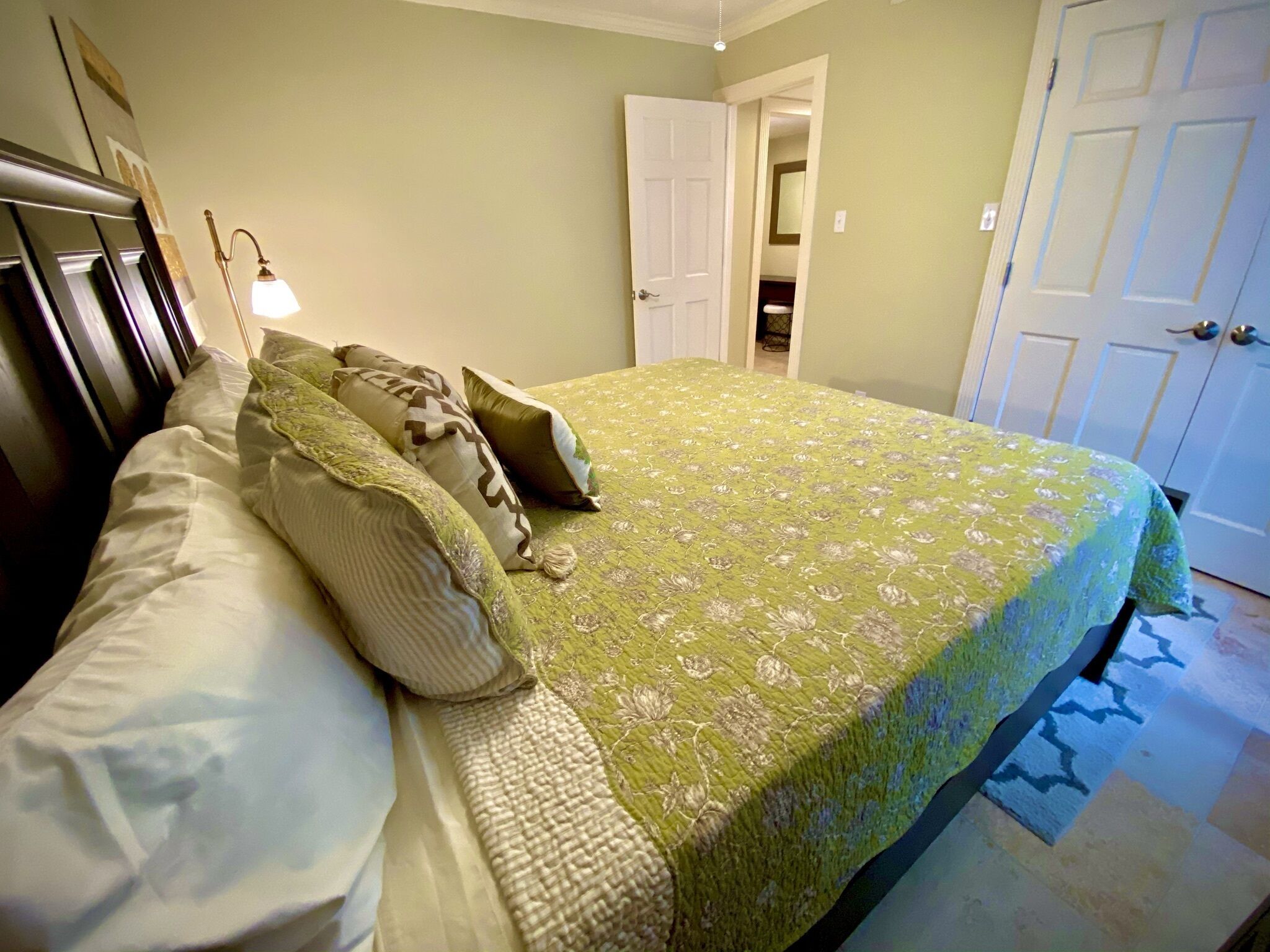 A bedroom with a bed, pillows, a lamp, and a door.