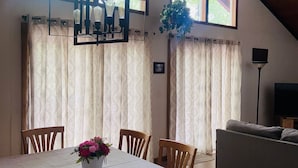 A dining area with a table set for four, wooden chairs, a chandelier, and a view through large windows. - Book for Winter and Spring!  Great rates! Family and dog friendly! (Lake Harmony)