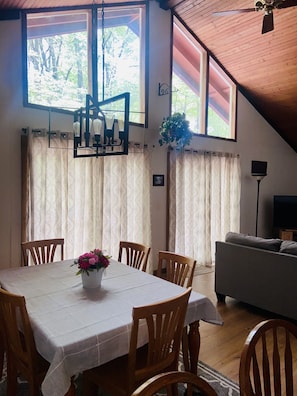A dining area with a table set for four, wooden chairs, a chandelier, and a view through large windows. - Book for Winter and Spring!  Great rates! Family and dog friendly! (Lake Harmony)