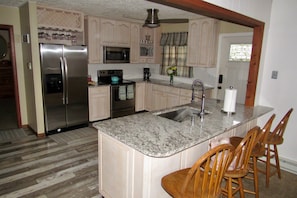 A kitchen with a stainless steel refrigerator, microwave, and oven, a granite countertop, wooden chairs, and a window with curtains. - Book for Winter and Spring!  Great rates! Family and dog friendly! (Lake Harmony)