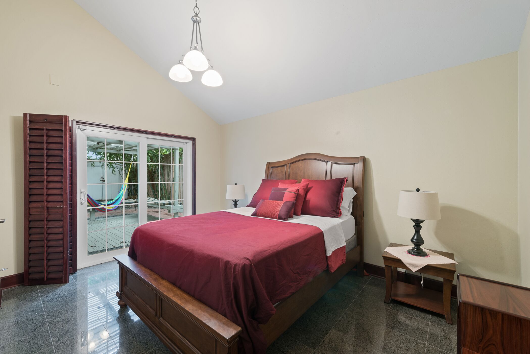A bedroom with a large bed, a wooden headboard, a nightstand with a lamp, and a sliding glass door leading to a balcony.