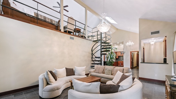 A spacious living area with a curved sectional sofa, a wooden coffee table, and a spiral staircase leading to an upper level. - Exquisite house with loft . Great deals for longer stays (Houston)