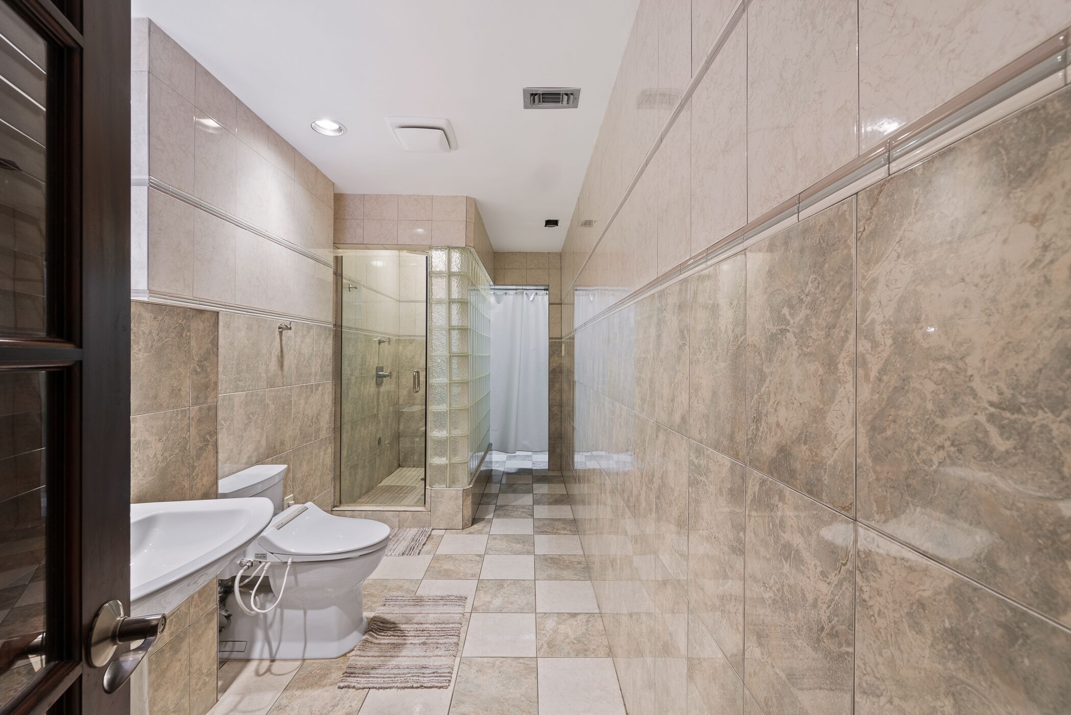 A modern bathroom with a glass shower enclosure, a toilet, and a bidet.