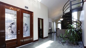 A spacious hallway with a polished stone floor, a grand wooden door with glass panels, and a spiral staircase with a black metal railing. - Exquisite house with loft . Great deals for longer stays (Houston)