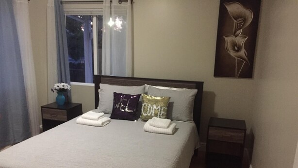 A neatly made bed with two pillows, a vase with flowers, and a decorative wall piece.
