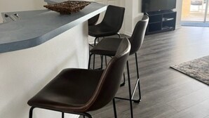 Een moderne keuken met een bar, een eethoek met stoelen, en een televisie op de achtergrond.