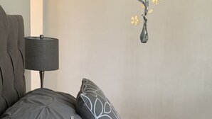 Een slaapkamer met een bed, kussens, een lamp en wanddecoratie.