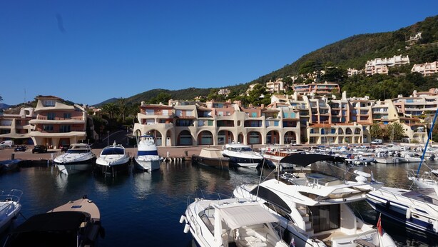 A marina with several yachts docked, surrounded by multi-story buildings with balconies and arched windows. - sea ​​view Apartment Direct access private beach, swimming pools, sauna, hammam, tennis etc. (Théoule-Sur-Mer)