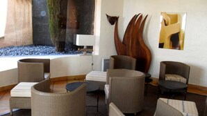 A lounge area with wicker furniture, a stone wall, and a large abstract art piece. - sea ​ ​view Apartment Direct access private beach, swimming pools, sauna, hammam, tennis etc. (Théoule-Sur-Mer)