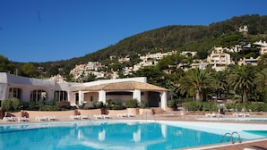 A pool area with a clear blue pool, white lounge chairs, and a building with a tiled roof. - sea ​​view Apartment Direct access private beach, swimming pools, sauna, hammam, tennis etc. (Théoule-Sur-Mer)
