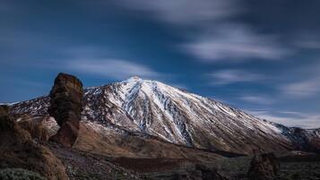 Una montaña con una formación rocosa destacada en primer plano y un pico nevado al fondo.