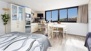 A modern hotel room with a bed, a kitchenette, a dining area, and a large window offering a view of the outdoors. - Cozy studio with breathtaking sea and Teide views, quiet neighborhood. (LA GUANCHA)