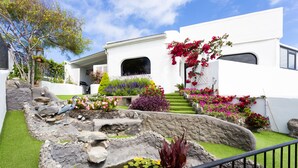 A modern white house with a well-maintained garden, including a pond, various plants, and a staircase leading to the entrance. - Cozy studio with breathtaking sea and Teide views, quiet neighborhood. (LA GUANCHA)