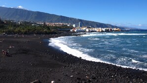 A beach with a mountain in the background, rocky shoreline, and buildings along the coast. - Cozy studio with breathtaking sea and Teide views, quiet neighborhood. (LA GUANCHA)