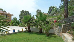 A well-maintained garden with palm trees, a stone wall, and a building in the background.