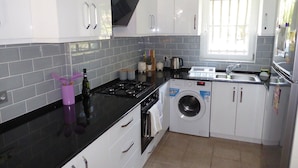 A modern kitchen with white cabinets, a black countertop, a built-in washing machine, and a window providing natural light.
