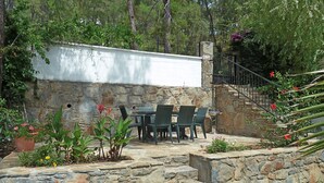 A stone patio with a table and chairs, surrounded by potted plants and flowers.