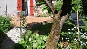Un jardin avec une terrasse en bois, un mur en pierre et une porte rouge.