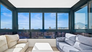 A modern living room with a white coffee table, two sofas, and large windows offering a city view.