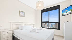 A modern hotel room with a large bed, a nightstand, a desk, a flat-screen TV, and a window with a city view.