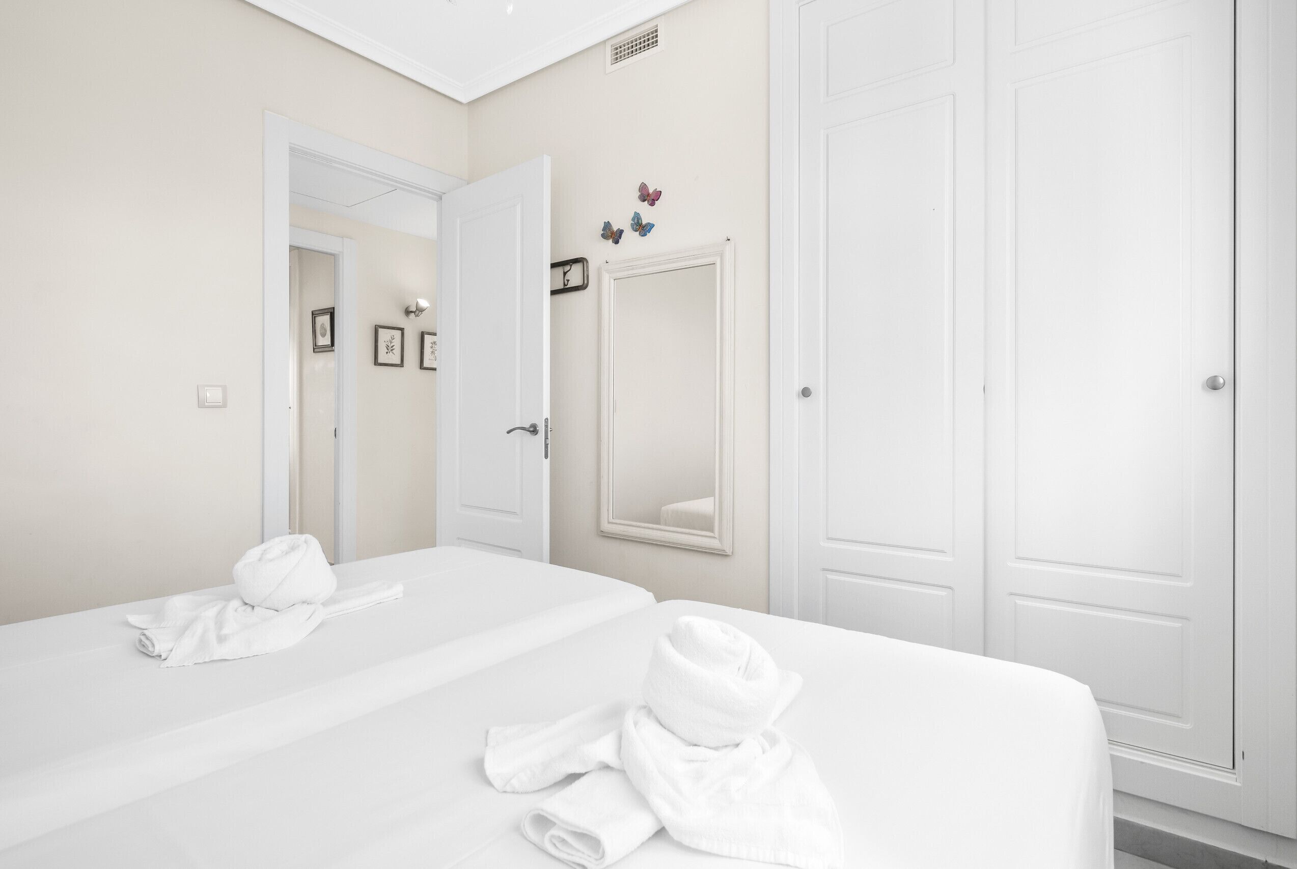 A hotel room with two beds, a large mirror, and white walls.