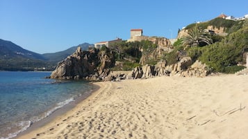 Une plage avec une eau d’un bleu limpide, un rivage sablonneux, des falaises rocheuses et des bâtiments construits sur le flanc de la colline.