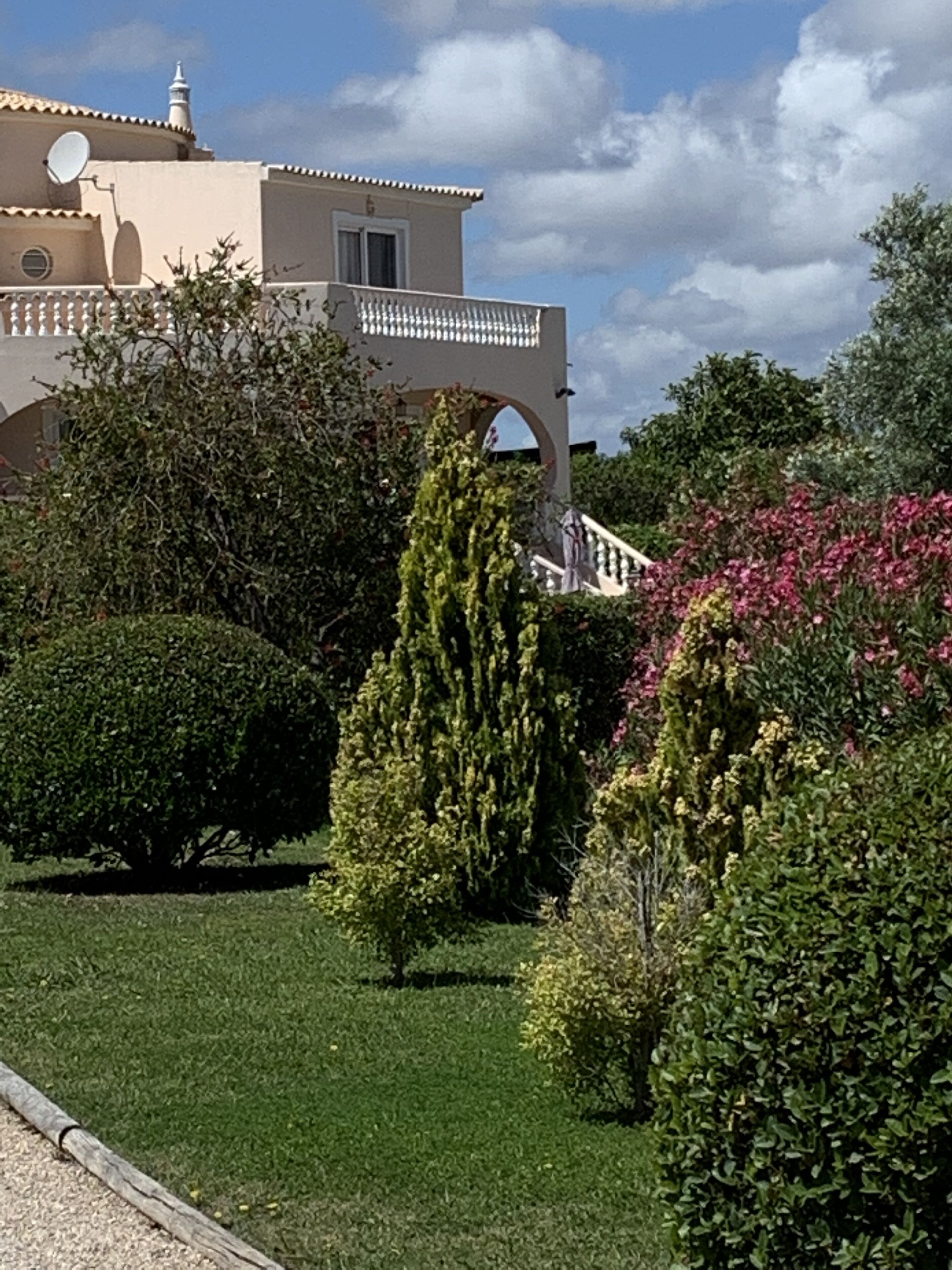 Un bâtiment de couleur beige doté d’un balcon, entouré de haies et d’arbres bien entretenus.