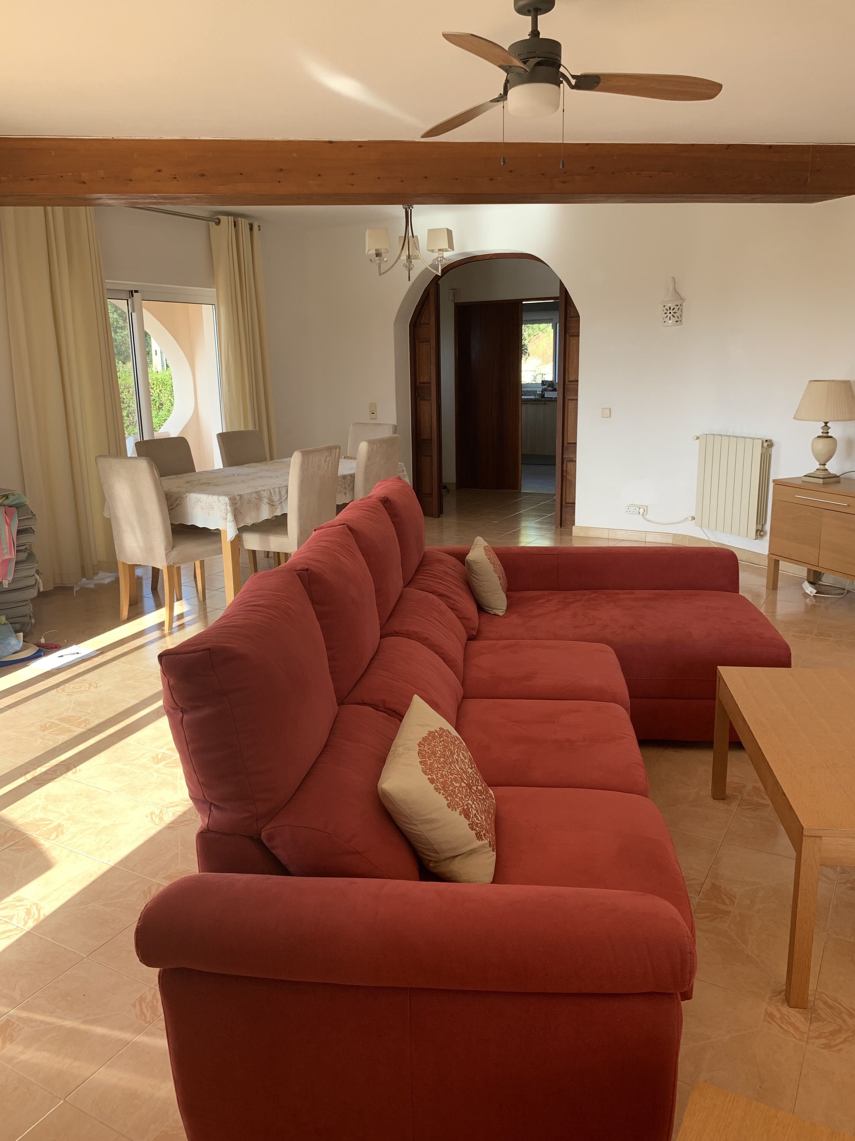 A spacious living room with a large red sectional sofa, a wooden coffee table, and a ceiling fan.