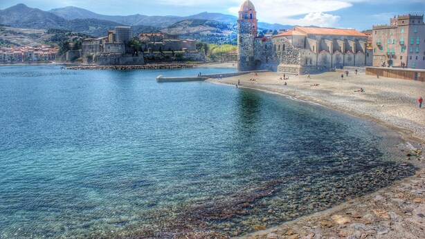 Un pueblo costero con una fortaleza histórica, aguas cristalinas y una playa de arena.