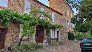 Un edificio de piedra con una torre redonda, arcos en las entradas y contraventanas blancas.