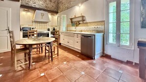 Una cocina con techo de piedra, armarios blancos, una mesa de comedor de madera y un ventanal con vistas.