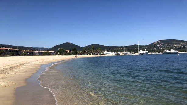 A beach with clear water, sandy shore, and buildings in the background. - Fully renovated air-conditioned cabin close to the beach (Port Grimaud)
