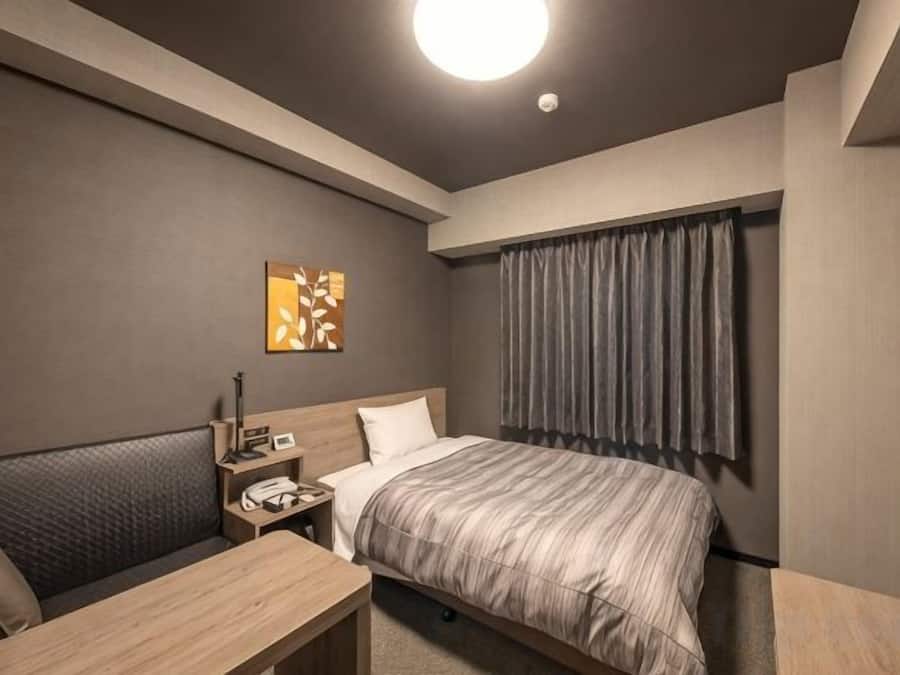 Habitació d'hotel amb llit, tauleta de nit, làmpada i un quadre a la paret.