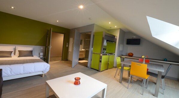 A modern hotel room with a bed, a desk, and a kitchenette.