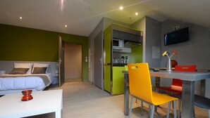 A modern hotel room with a bed, a desk, a chair, a TV, and a kitchenette. - Residence Appart'en Ville - studio 2 people (Saint-Flour)