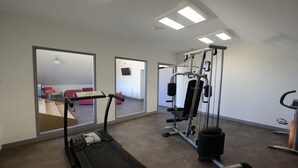 Ein Fitnessstudio mit Laufband, Kraftgeräten und einer Spiegelwand.