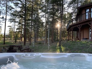 A hot tub in a forested area with a wooden cabin in the background.