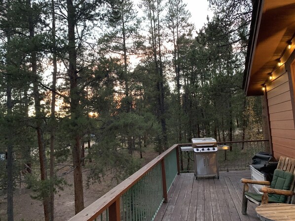 A deck with a grill and outdoor furniture, surrounded by tall trees.