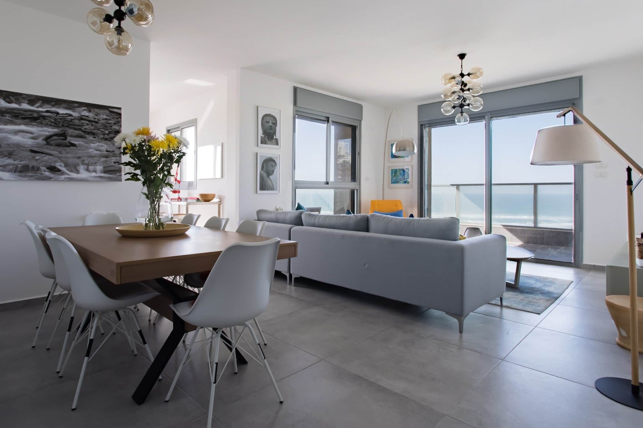 A modern living room with a dining area, grey sofa, and a view of the ocean.