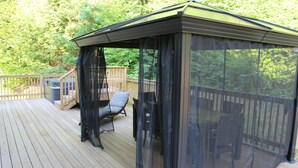 Een overdekt terras met een houten dek, een comfortabele stoel en een tafel.