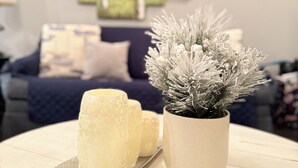 Een woonkamer met een witte tafel, een plant in een pot en een decoratief glazen object.