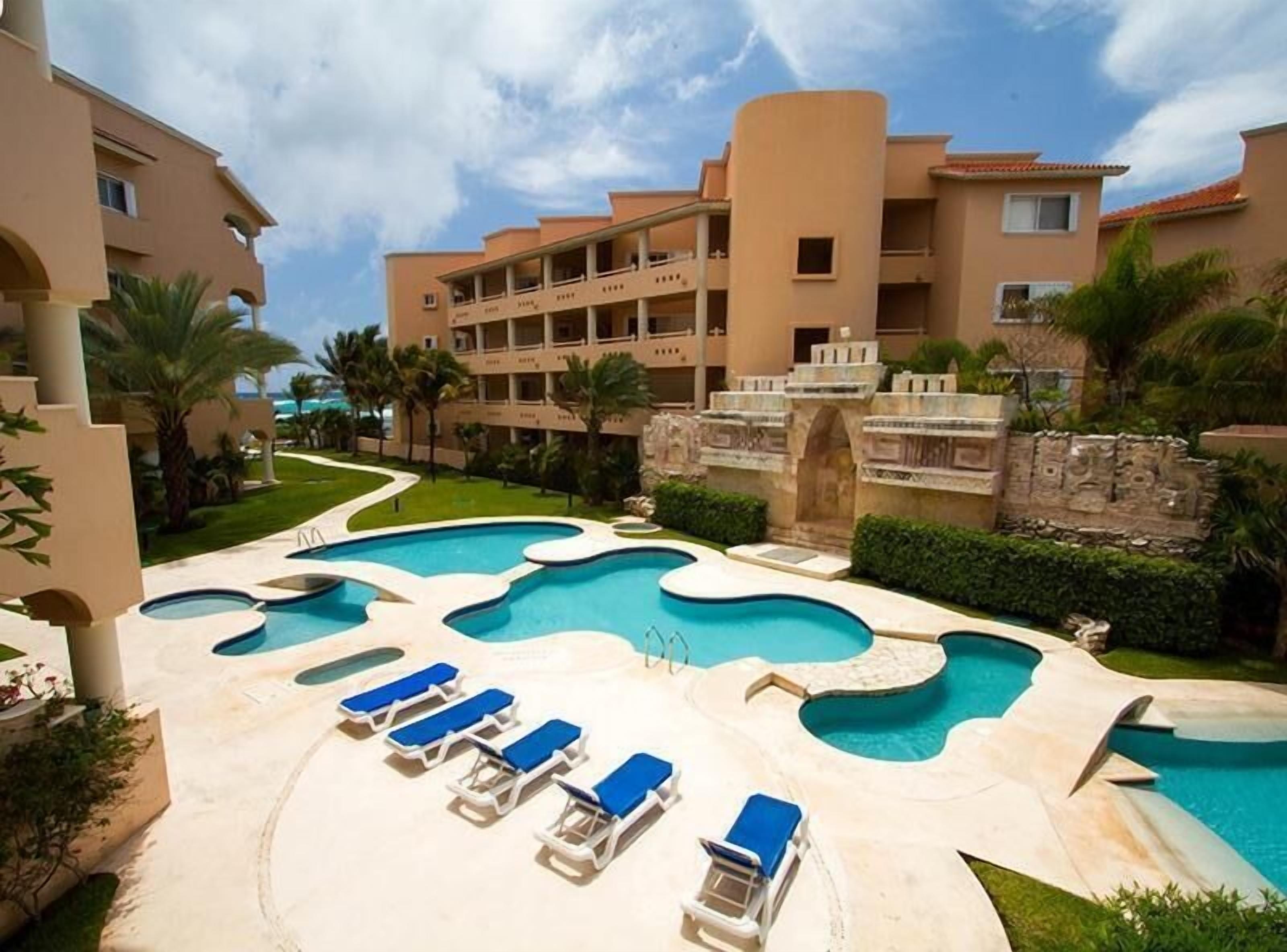 A resort with a pool area, multiple lounge chairs, and a building with balconies.