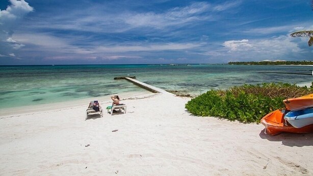 A beach with two lounge chairs and a small boat on the sand. - Quinta Del Sol, 3 Bedroom Beachfront Condo In Puerto Aventuras, Riviera Maya (puerto aventuras)