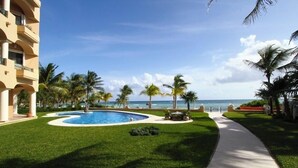 A swimming pool surrounded by palm trees and a clear view of the ocean. - Quinta Del Sol, 3 Bedroom Beachfront Condo In Puerto Aventuras, Riviera Maya (puerto aventuras)
