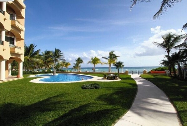 A swimming pool surrounded by palm trees and a clear view of the ocean.