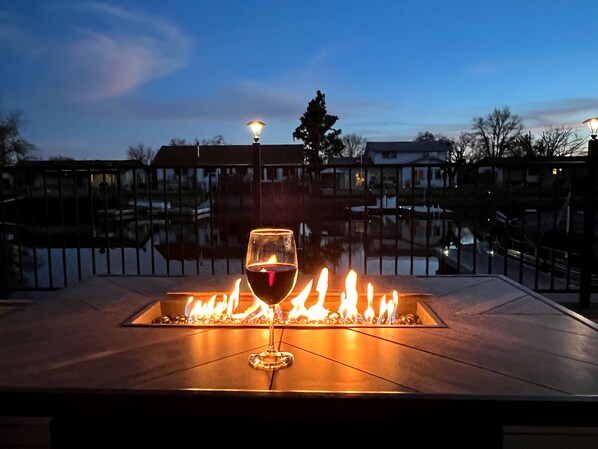 A glass of red wine on a fire pit with a view of a residential area at dusk.