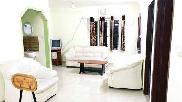 A living room with a sofa, armchairs, a coffee table, a TV, and a clock on the wall. - Noise free home stay (Eranakulam)