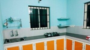 A kitchen with white and orange cabinets, a black stove, and a window with metal bars. - Noise free home stay (Eranakulam)